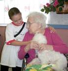 Girl hugging senior citizen petting a dog links to Pet Therapy.